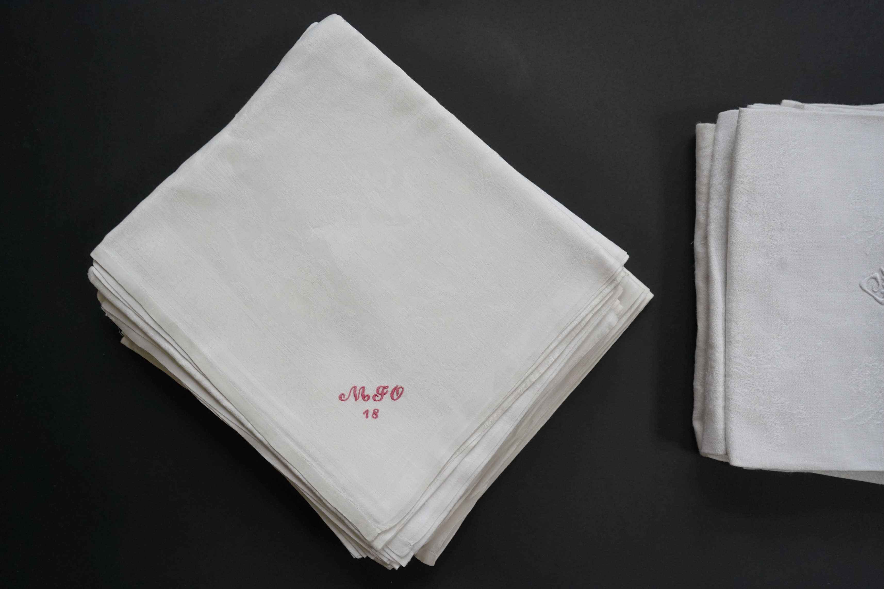 A set of nine red monogrammed 19th century large damask dinner napkins and a similar set of coarser French provincial damask napkins, the large set, decoratively designed with a boating river scene, amongst classical bui